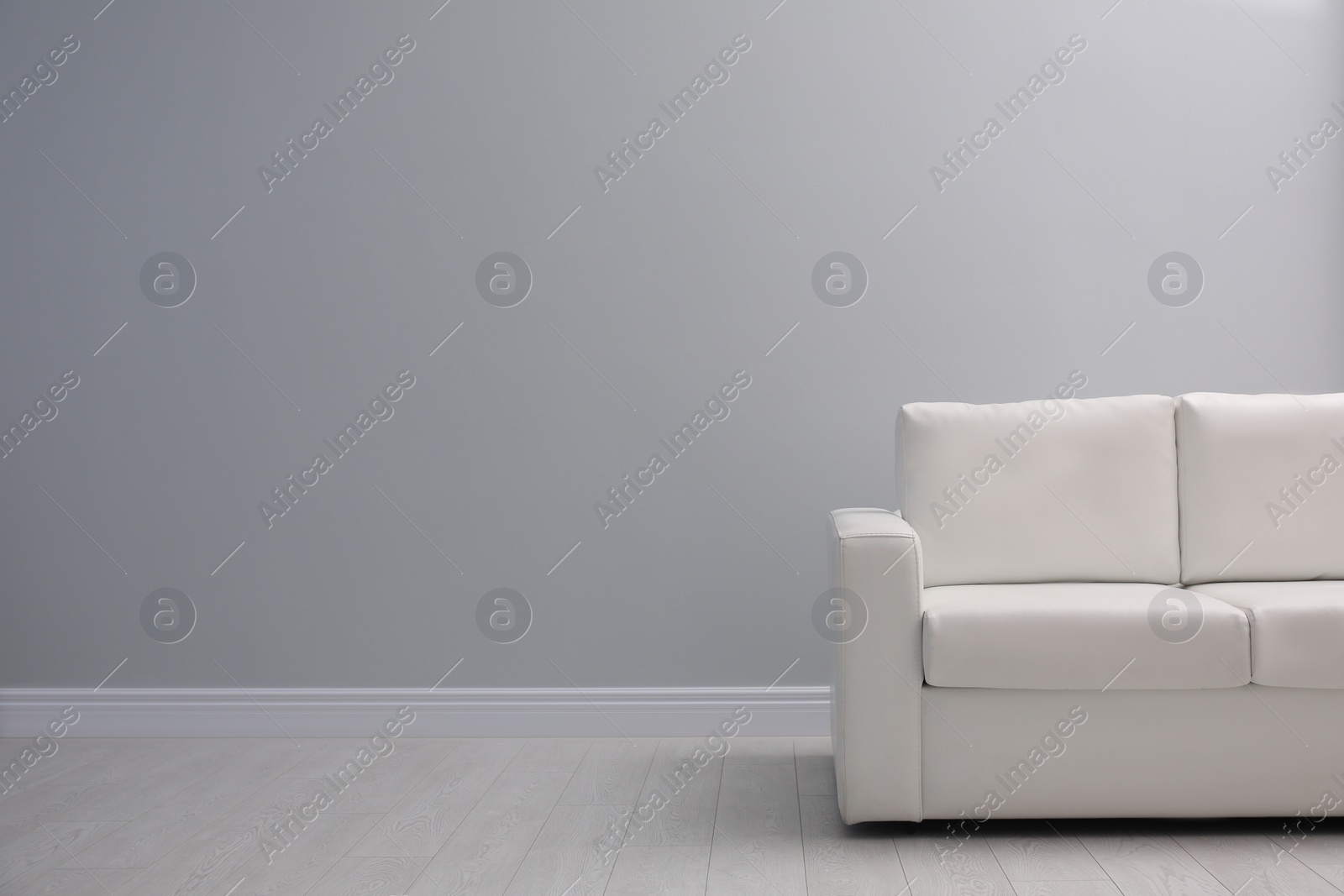 Photo of Comfortable white sofa near light wall indoors, space for text. Simple interior