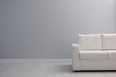 Photo of Comfortable white sofa near light wall indoors, space for text. Simple interior
