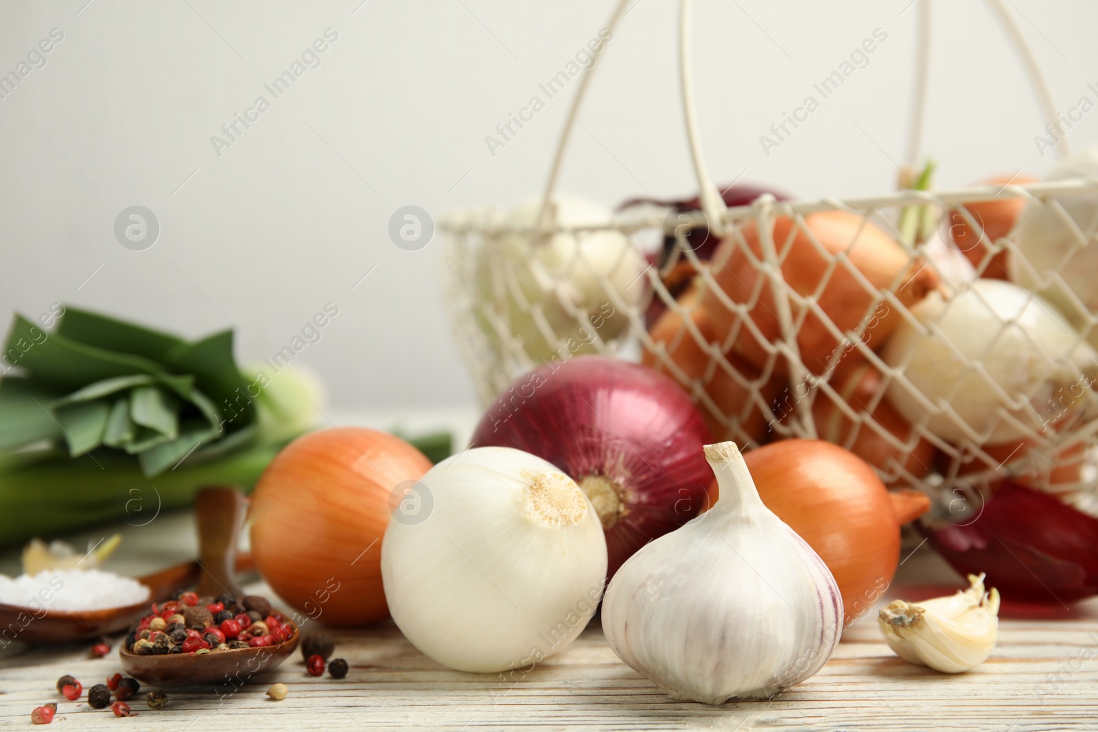 Photo of Fresh onion bulbs, leek, garlic, peppers mix and salt on white wooden table