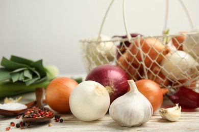 Photo of Fresh onion bulbs, leek, garlic, peppers mix and salt on white wooden table