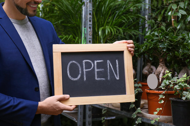 Male business owner holding OPEN sign in his flower shop, closeup