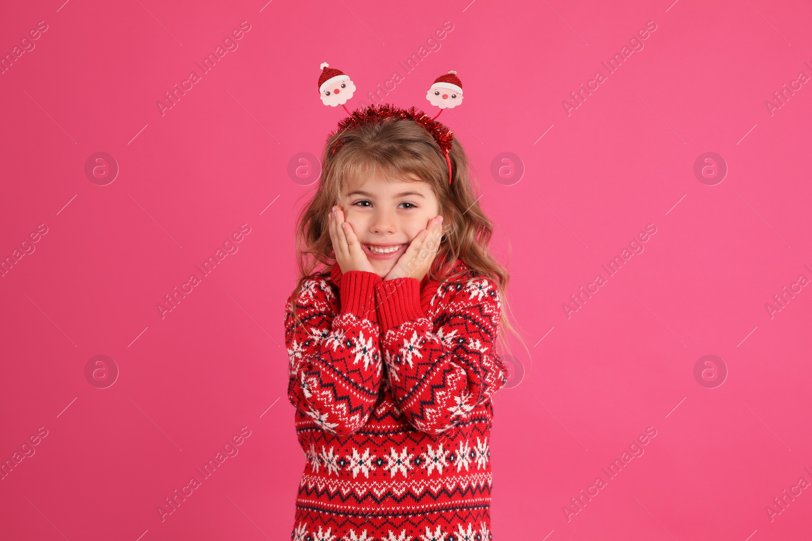 Photo of Cute little girl in red Christmas sweater smiling against pink background