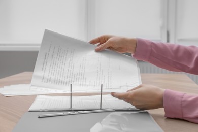 Photo of Woman putting punched pocket with document into folder at wooden table, closeup