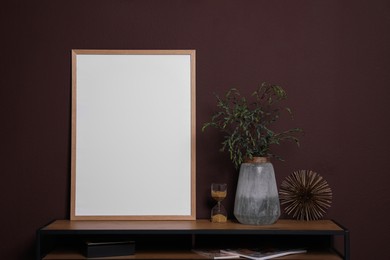 Photo of Empty frame with other decor on wooden console table near brown wall. Mockup for design
