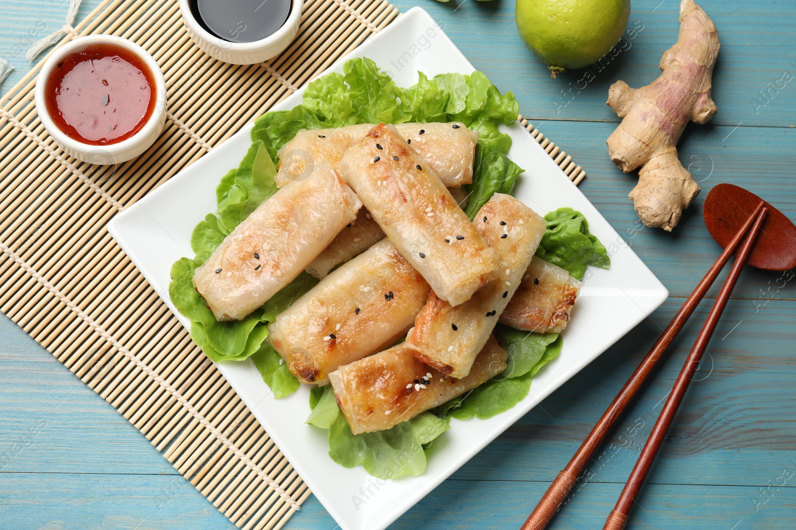 Photo of Tasty fried spring rolls, lettuce and sauces on light blue wooden table, flat lay