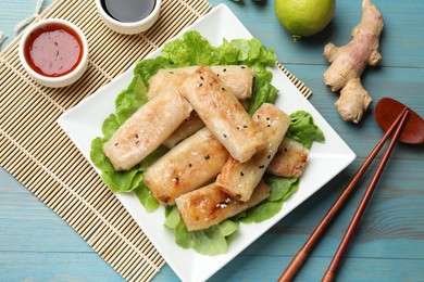 Photo of Tasty fried spring rolls, lettuce and sauces on light blue wooden table, flat lay