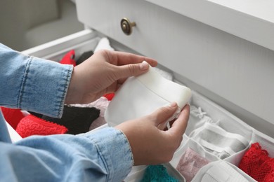 Photo of Woman folding beautiful panties above organizer with underwear in drawer, closeup