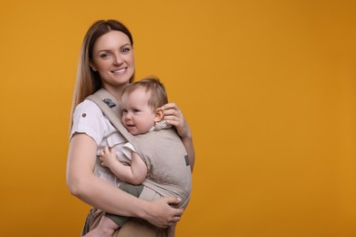 Photo of Mother holding her child in sling (baby carrier) on orange background. Space for text