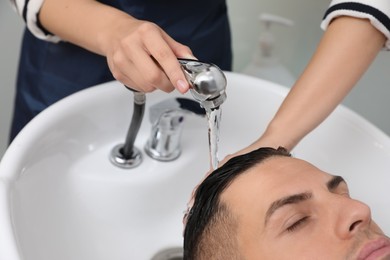 Photo of Professional hairdresser washing client's hair at sink indoors, closeup