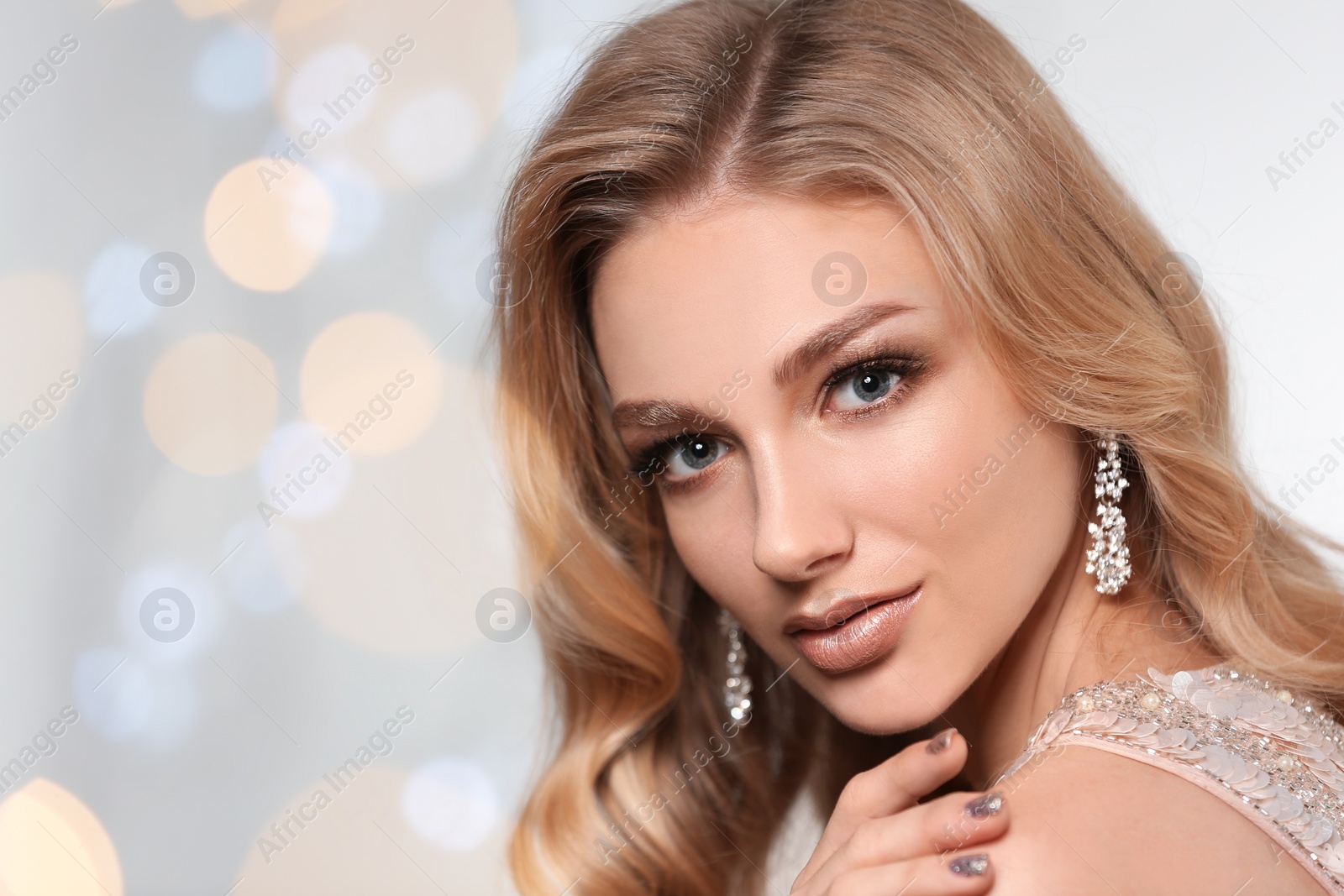 Photo of Beautiful young woman with elegant jewelry against defocused lights. Space for text