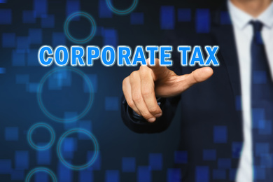 Image of Corporate tax concept. Man touching virtual screen on color background, closeup
