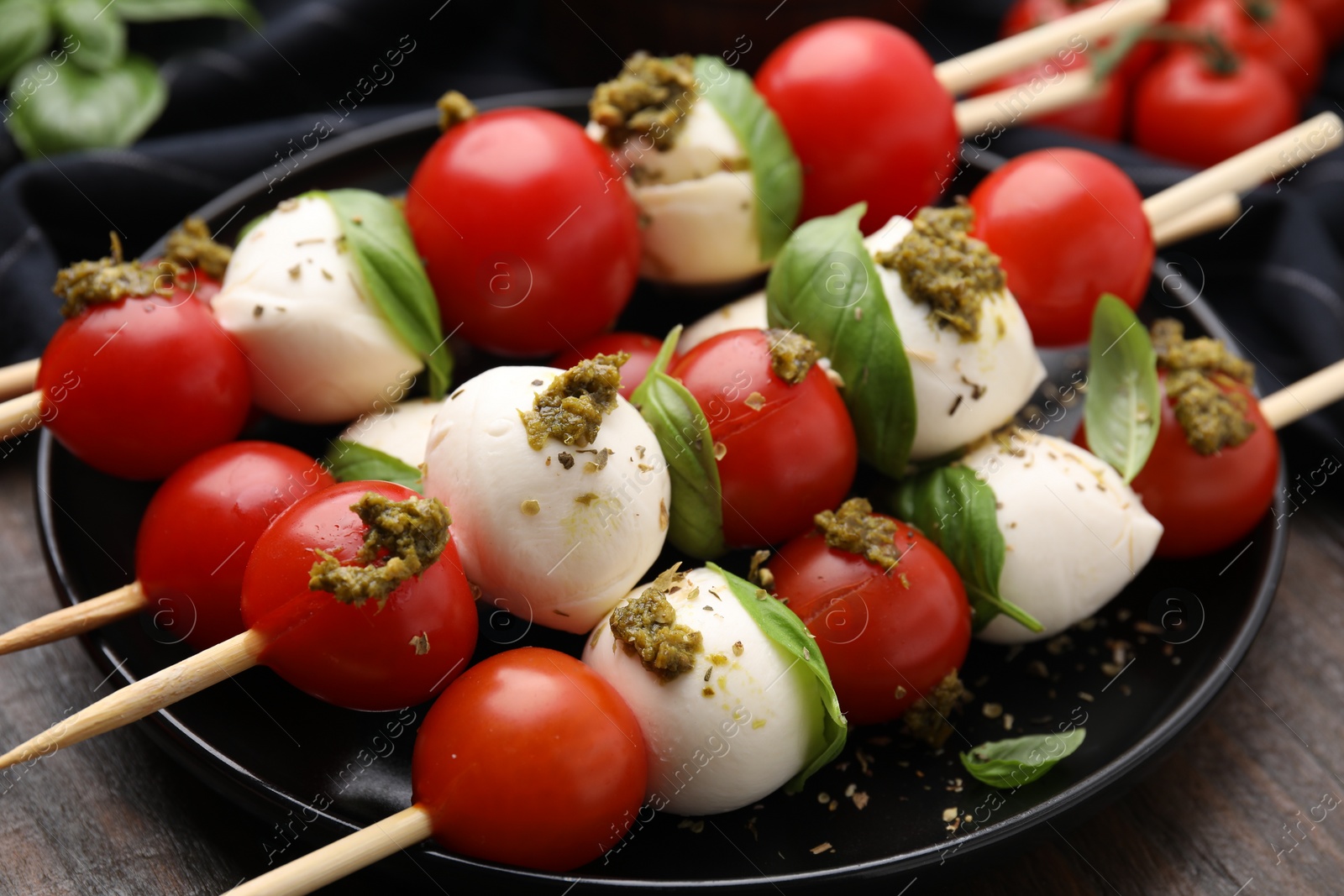 Photo of Caprese skewers with tomatoes, mozzarella balls, basil and pesto sauce on table, closeup