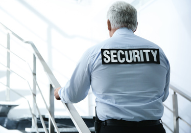 Professional security guard on stairs indoors, back view