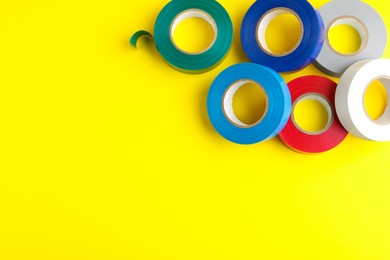 Photo of Colorful insulating tapes on yellow background, flat lay. Space for text