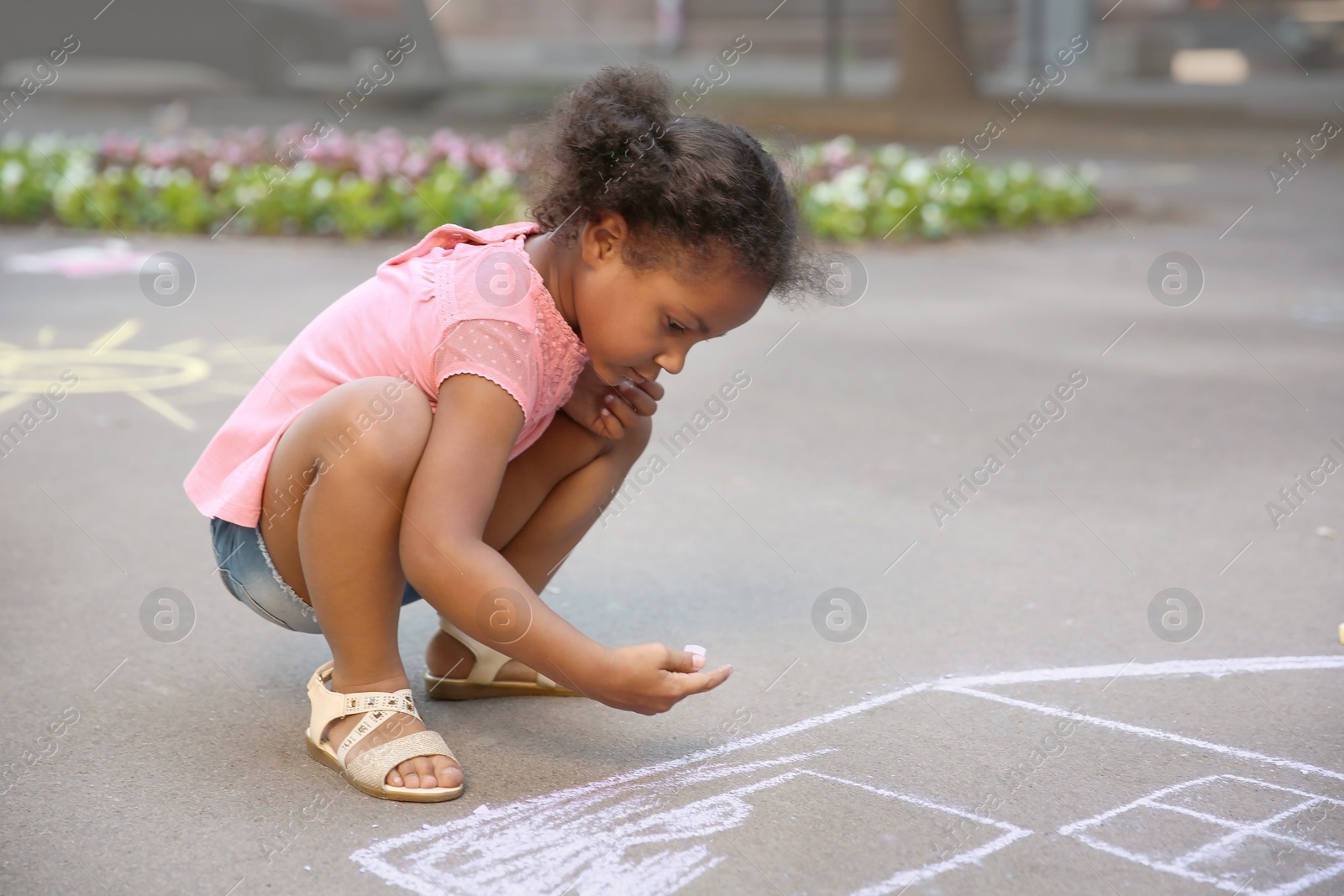 Photo of Little African-American child drawing house with chalk on asphalt