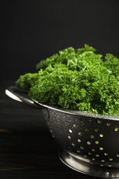 Photo of Colander with fresh green parsley on dark wooden table against black background, closeup