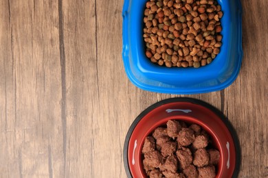 Dry and wet pet food in feeding bowls on wooden background, flat lay. Space for text