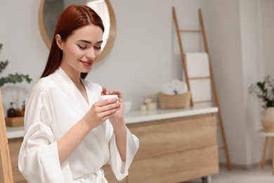 Photo of Beautiful young woman holding jar of body cream in bathroom, space for text