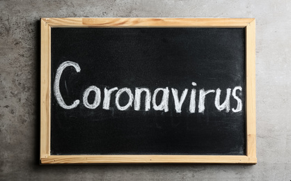 Photo of Blackboard with word CORONAVIRUS on light grey stone table, top view