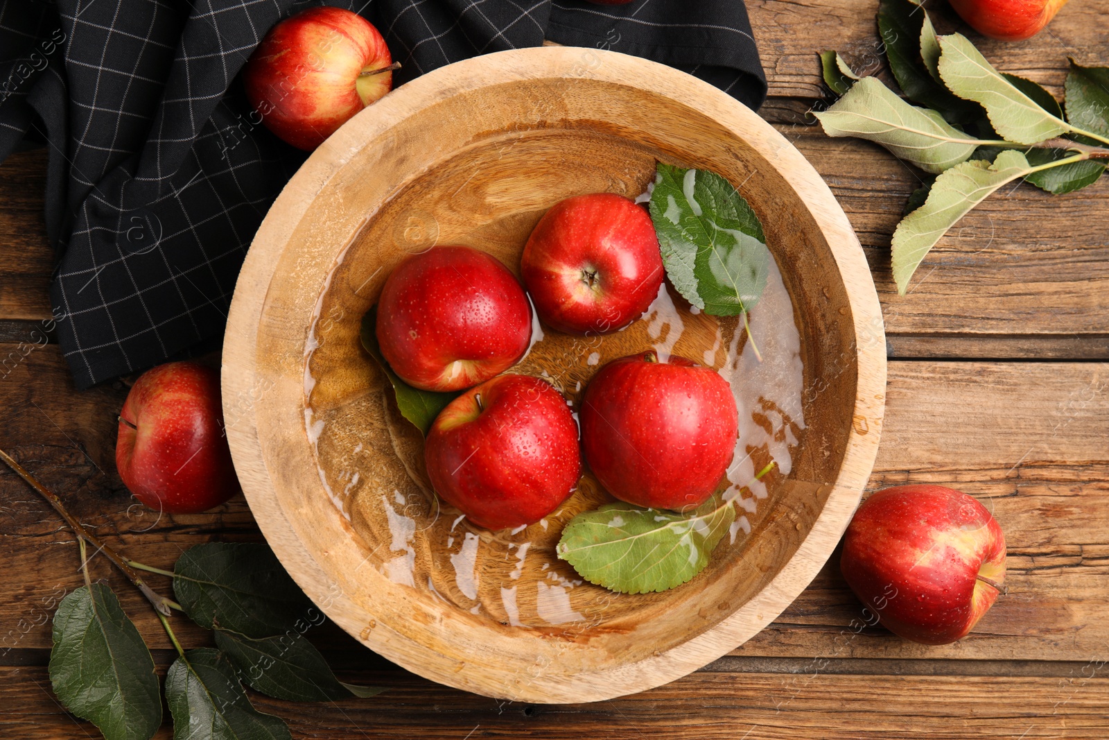 Photo of Ripe red apples in bowl of water on wooden table, flat lay