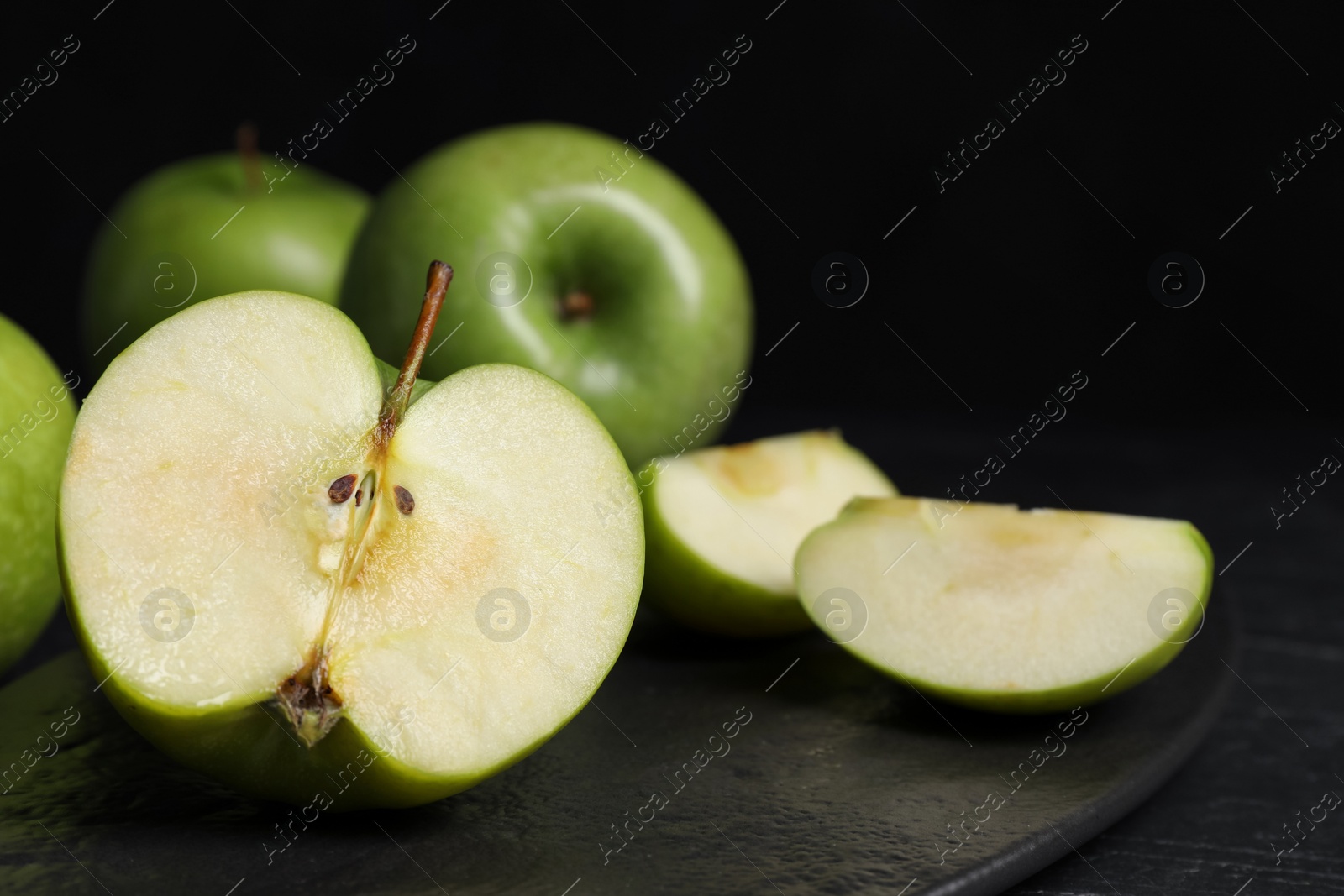 Photo of Cut and whole fresh green apples with slate plate on black table, closeup