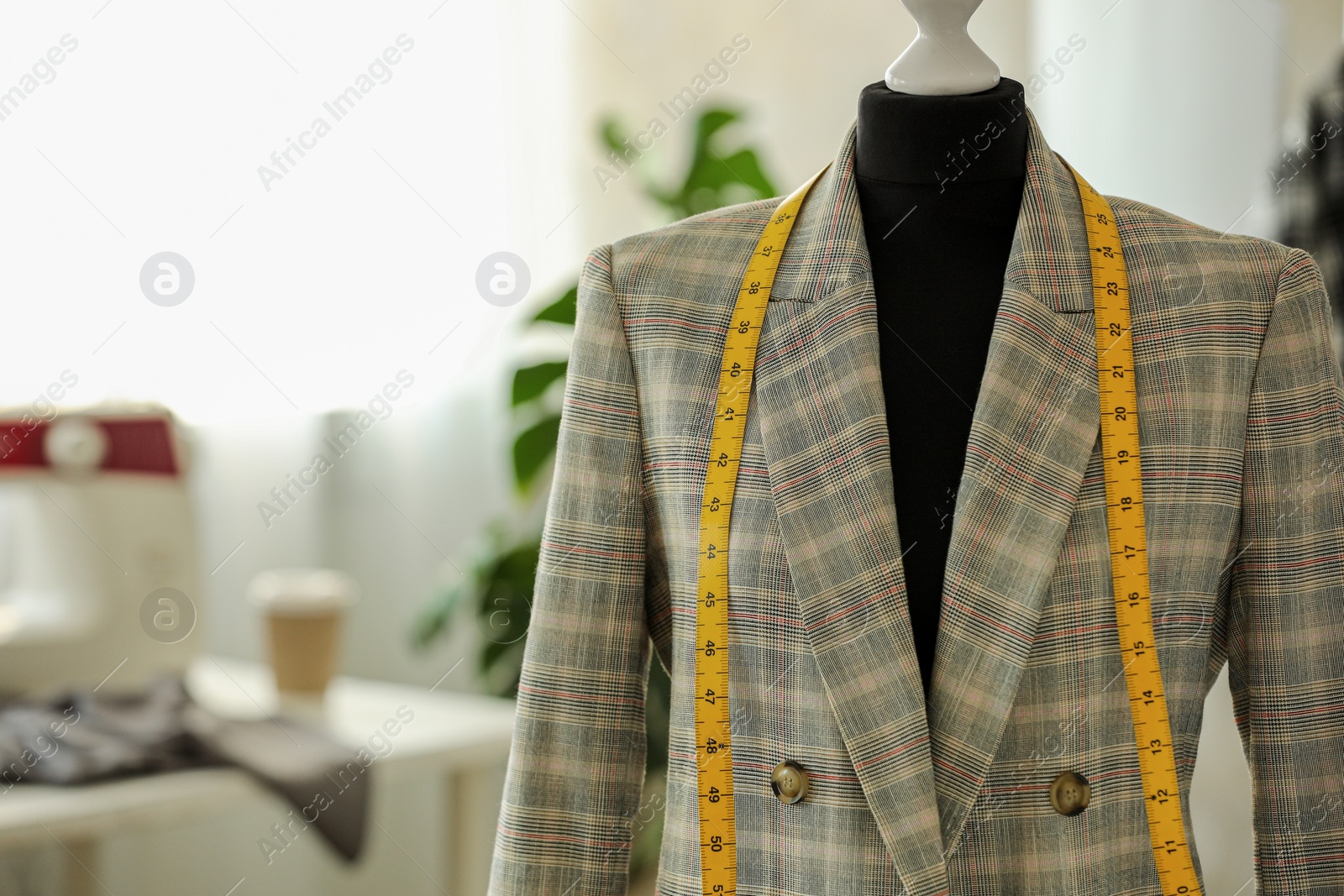 Photo of Mannequin with jacket and measuring tape in tailor shop, space for text