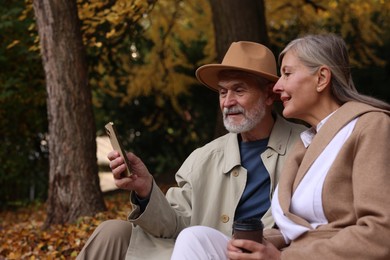 Photo of Affectionate senior couple using smartphone in autumn park