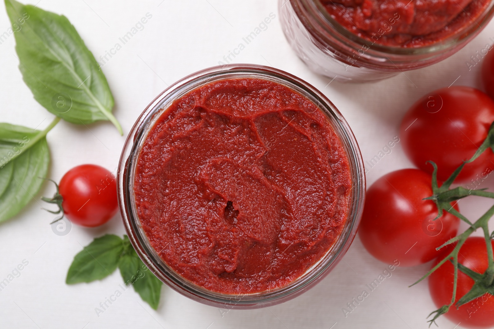 Photo of Jar of tasty tomato paste and ingredients on white table, flat lay