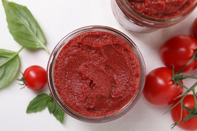 Jar of tasty tomato paste and ingredients on white table, flat lay