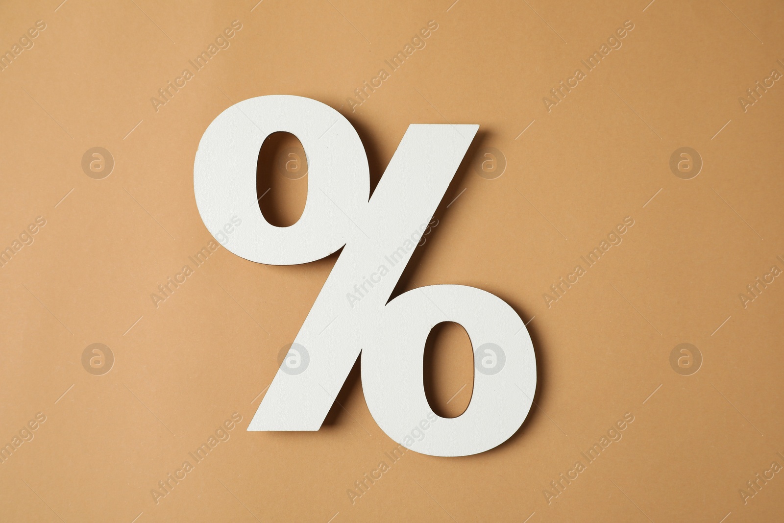 Photo of White percent sign on light brown background, top view