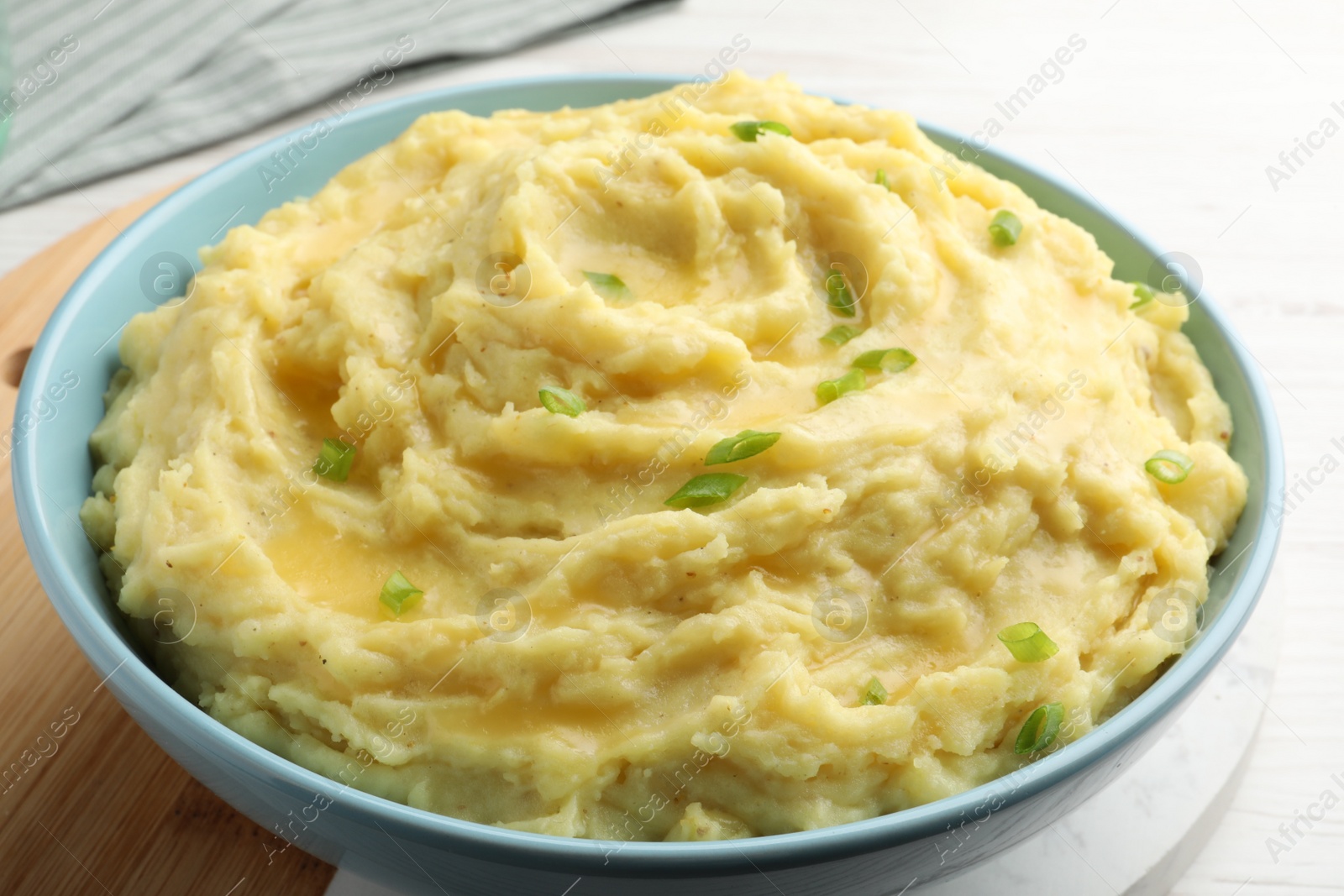 Photo of Bowl of tasty mashed potatoes with onion served on white wooden table, closeup