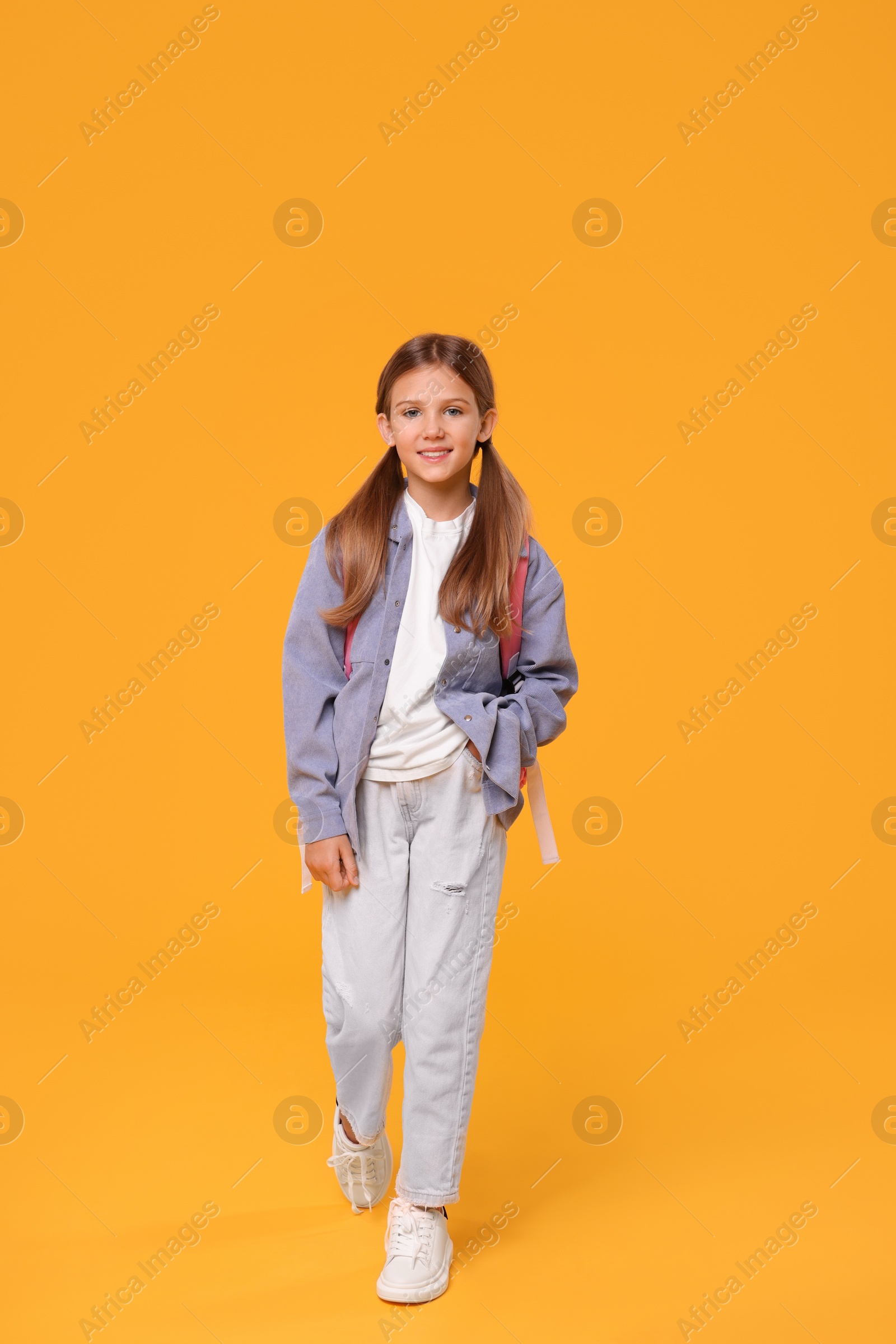 Photo of Happy schoolgirl with backpack on orange background