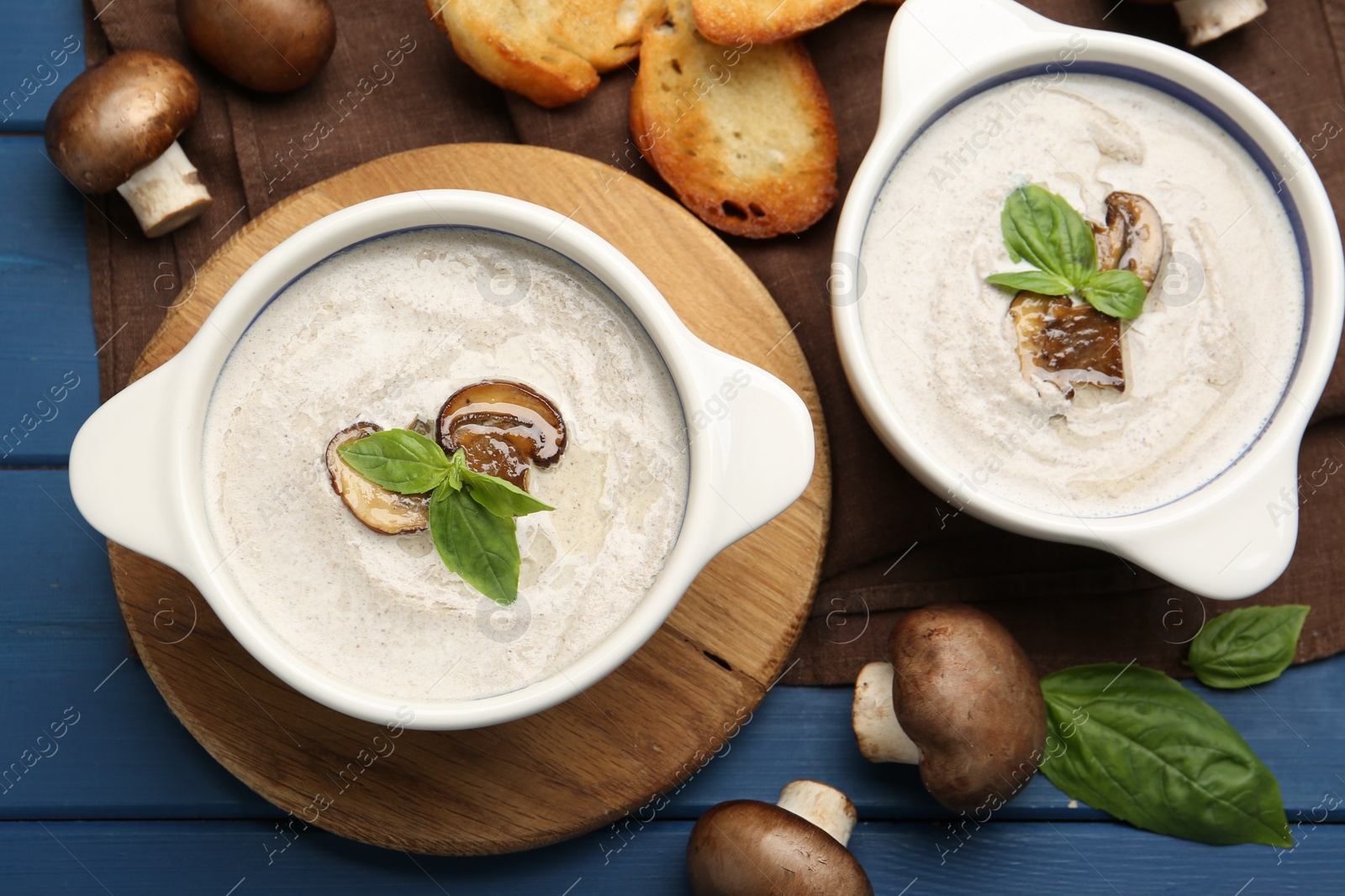 Photo of Delicious mushroom soup in ceramic pots and fresh ingredients on blue wooden table, flat lay