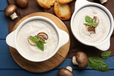 Delicious mushroom soup in ceramic pots and fresh ingredients on blue wooden table, flat lay