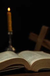 Photo of Church candle, Bible and cross on wooden table against black background