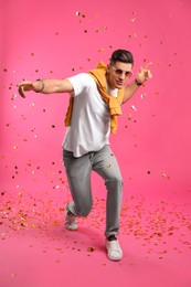 Photo of Happy man dancing and confetti on pink background