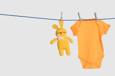 Baby onesie and toy bunny drying on laundry line against light background