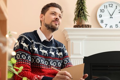 Photo of Man holding Christmas greeting card and pencil in living room