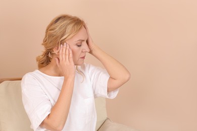 Woman suffering from headache near beige wall indoors. Hormonal disorders