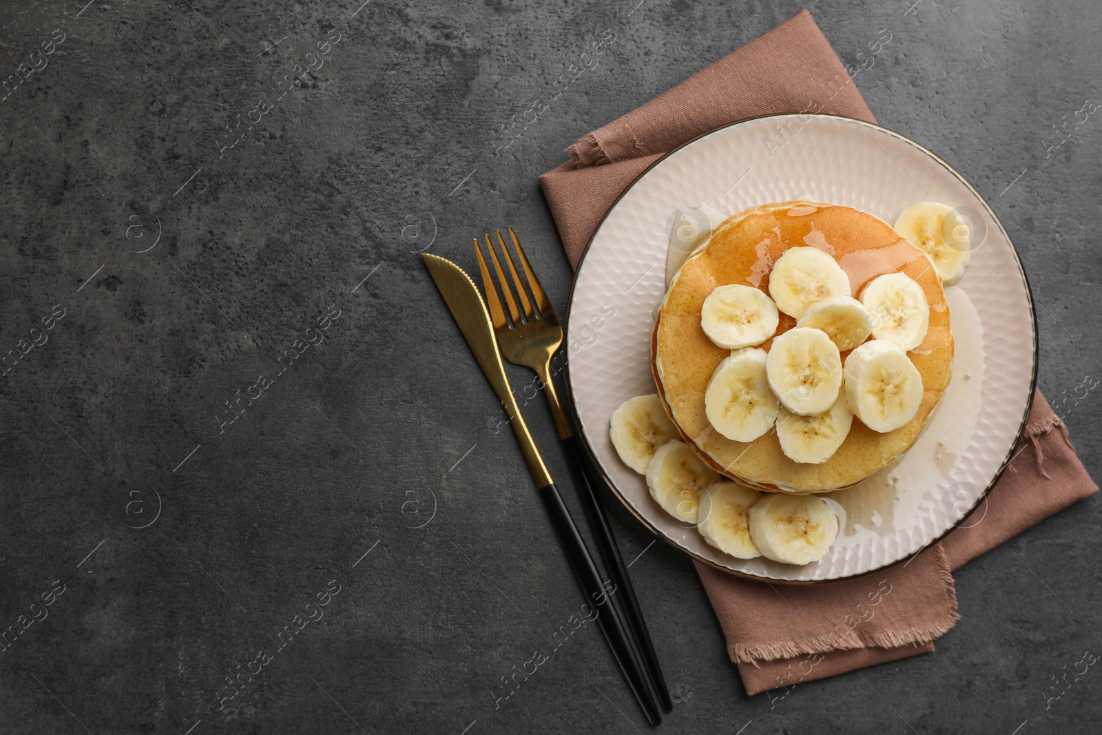 Photo of Tasty pancakes with sliced banana and honey served on gray table, flat lay. Space for text