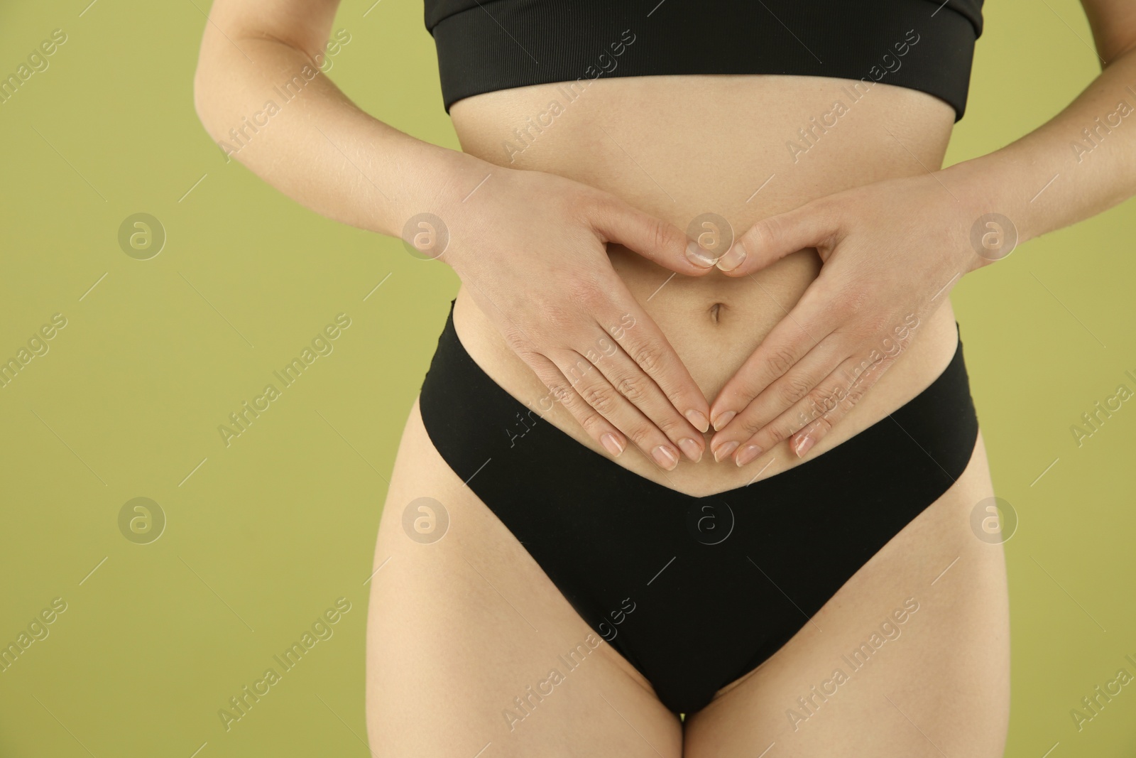 Photo of Gynecology. Woman in underwear making heart with her hands on green background, closeup