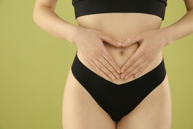 Gynecology. Woman in underwear making heart with her hands on green background, closeup