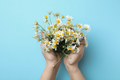 Photo of Woman holding chamomile bouquet on light blue background, top view