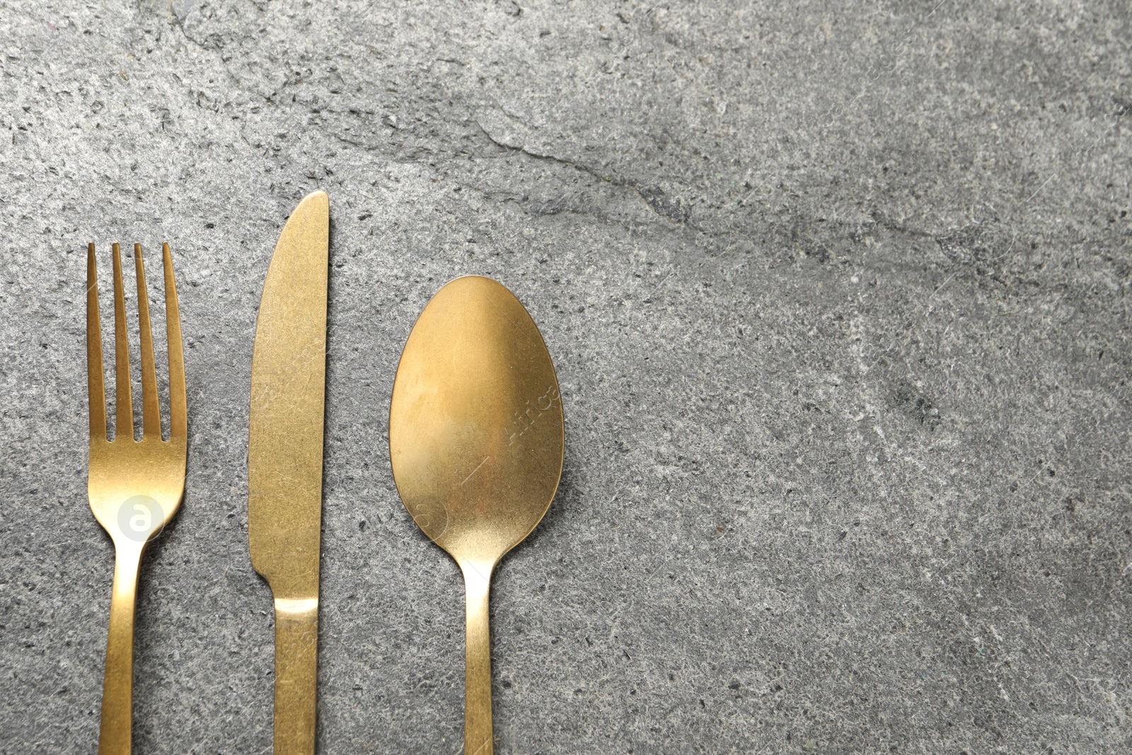 Photo of Stylish golden cutlery on grey table, flat lay. Space for text