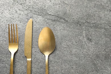 Photo of Stylish golden cutlery on grey table, flat lay. Space for text