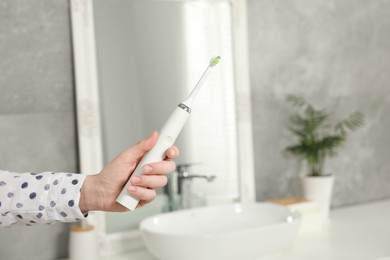 Woman holding electric toothbrush in bathroom at home, closeup