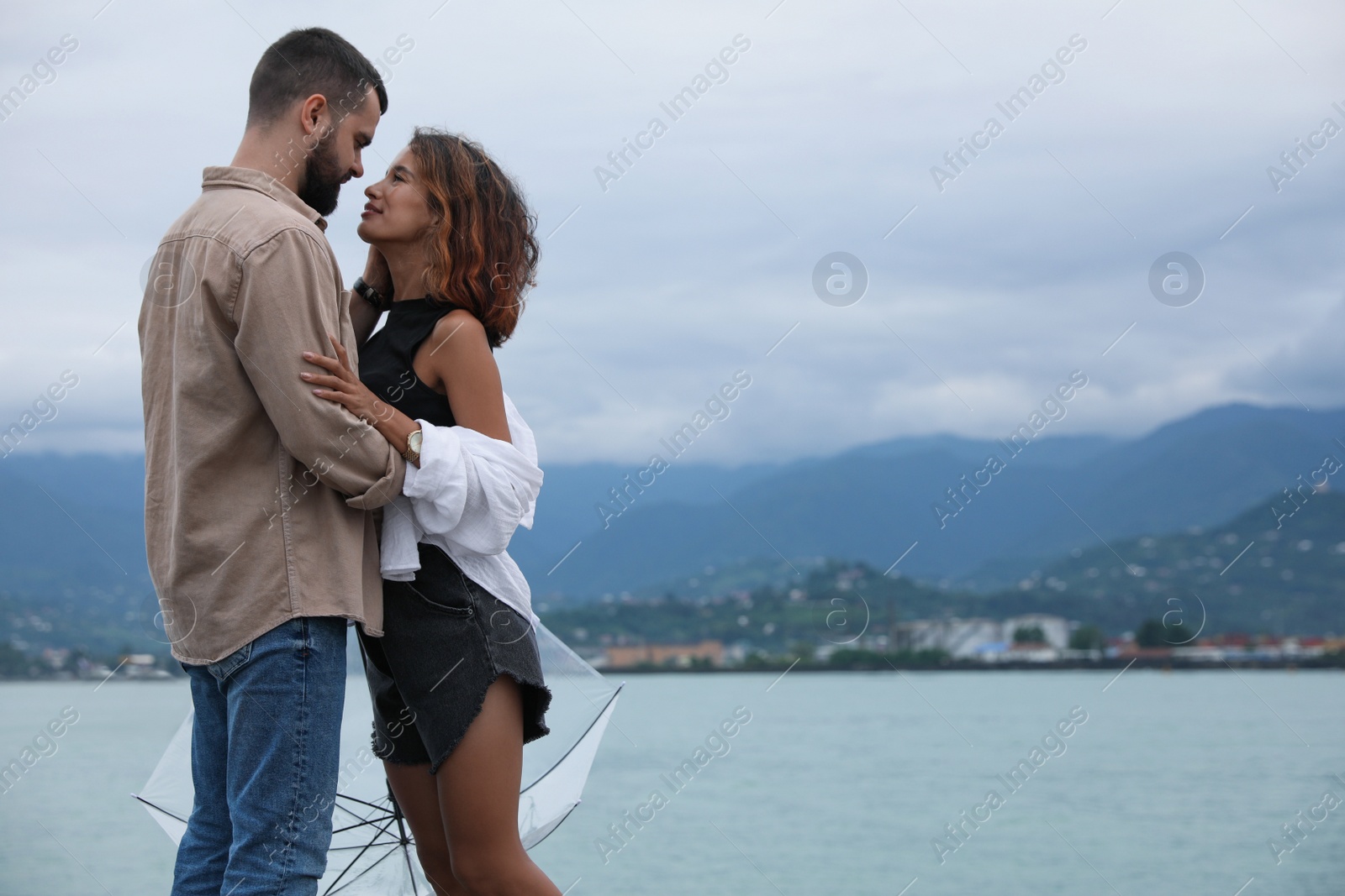 Photo of Young couple with umbrella enjoying time together under rain on beach, space for text