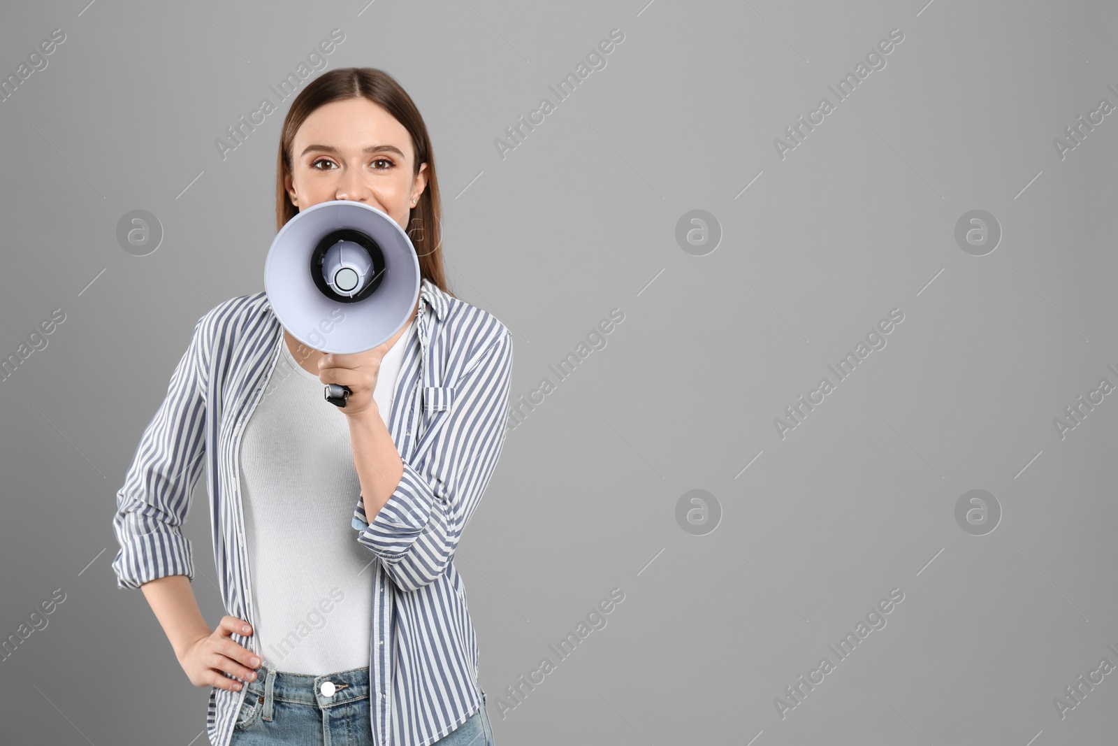 Photo of Young woman with megaphone on light grey background. Space for text