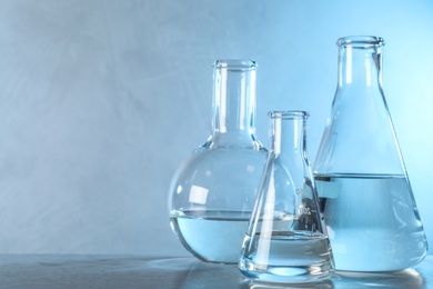 Laboratory glassware with liquid samples for analysis on table against toned blue background, space for text