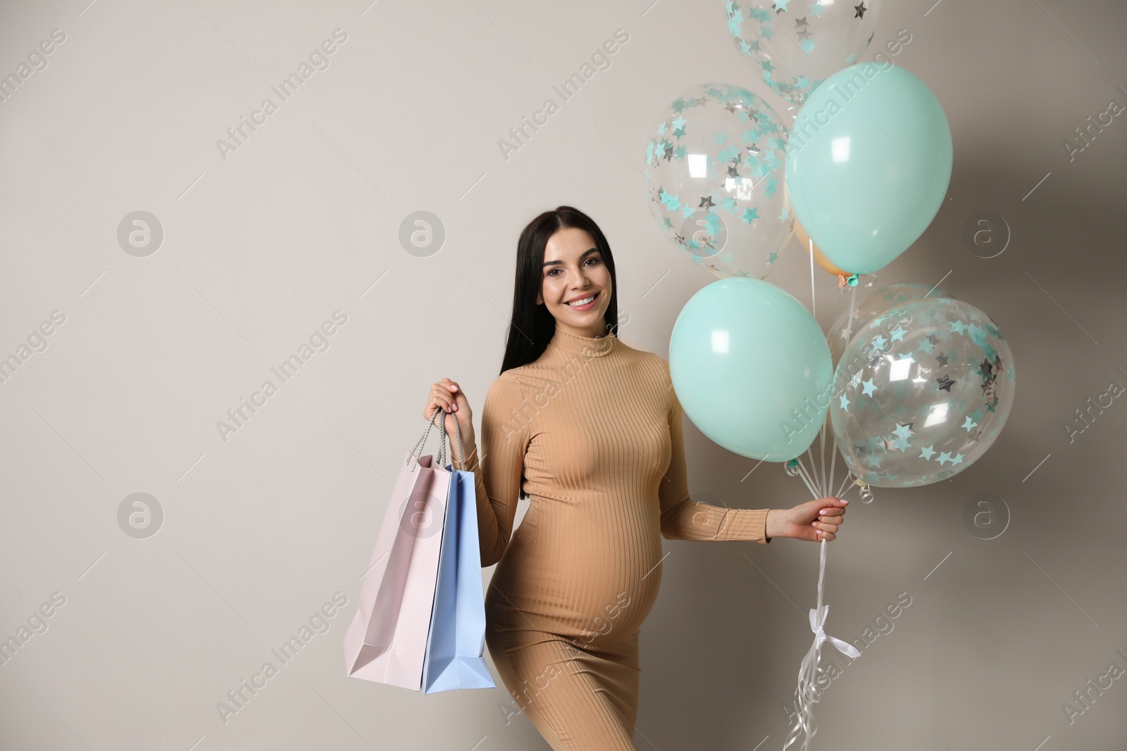 Photo of Happy pregnant woman with gifts and balloons near grey wall. Baby shower party